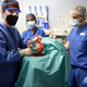 Four people in scrubs and PPE stand in an operating room. One is holding up a heart organ.